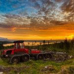 maquina forwarder da marca komatsu, cor vermelha, por do sol ao fundo do horizonte