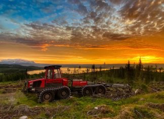 maquina forwarder da marca komatsu, cor vermelha, por do sol ao fundo do horizonte